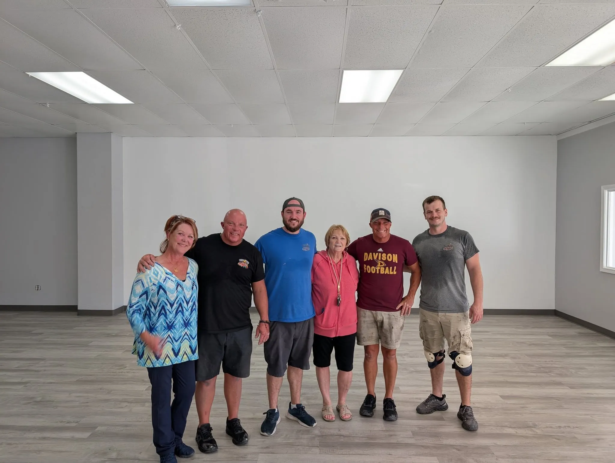 Six volunteers and family members standing together in the newly painted and floored HUB space.