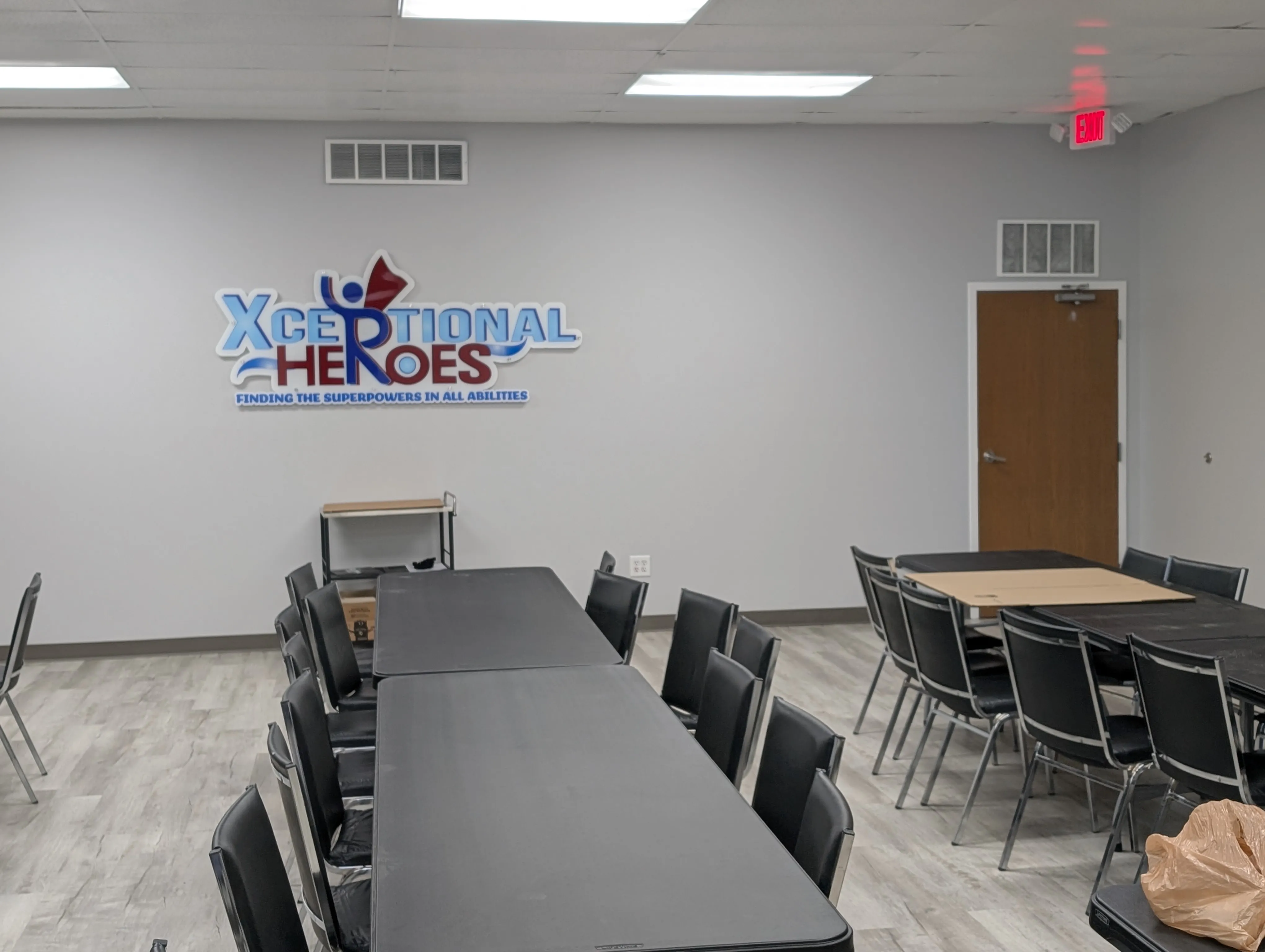 The HUB interior set up with rows of tables and chairs beneath the Xceptional Heroes logo mounted on the wall.