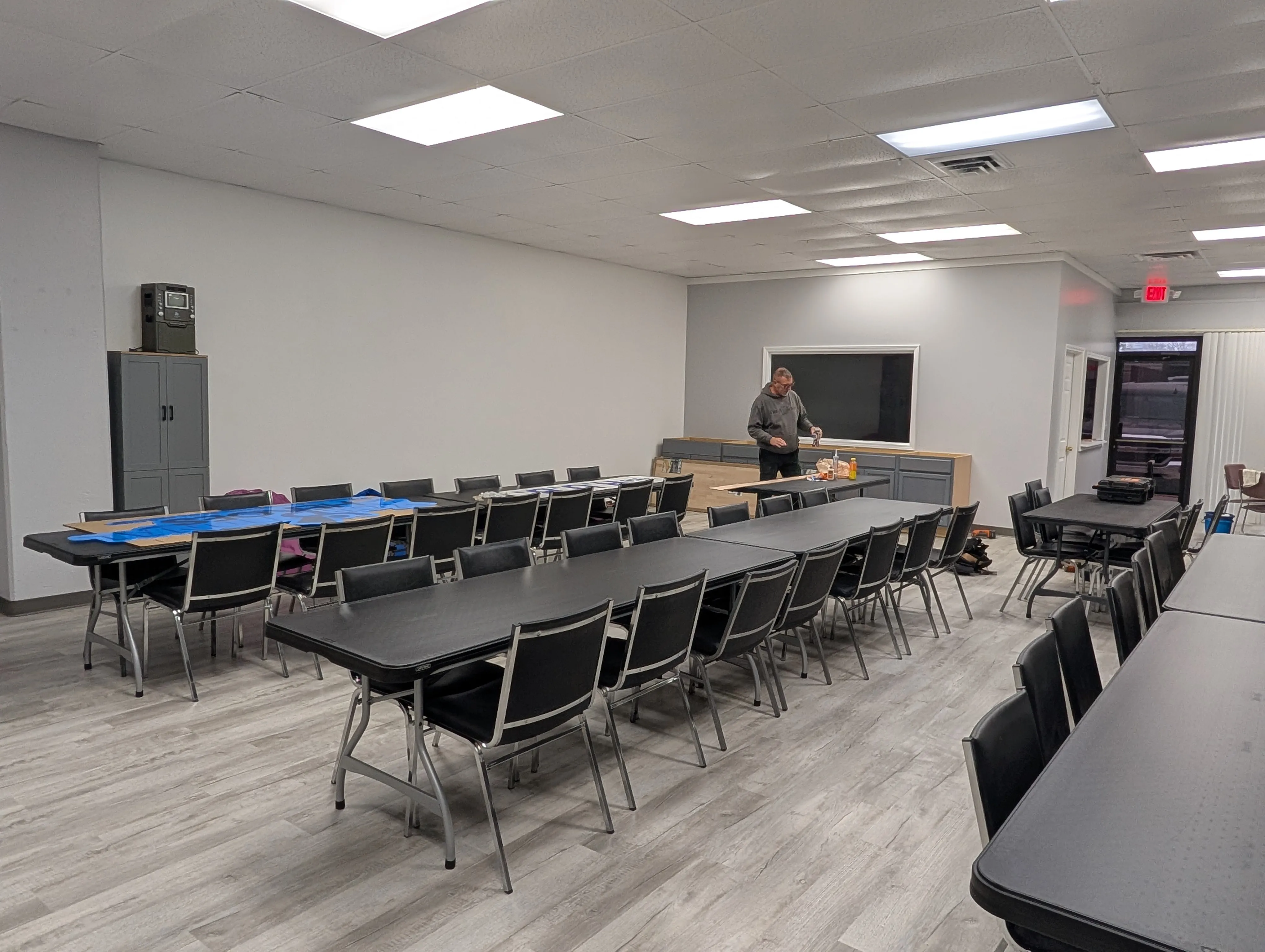 A wide view of the HUB room set up with tables and chairs, with the donated cabinet wall and pass-through window in the background.