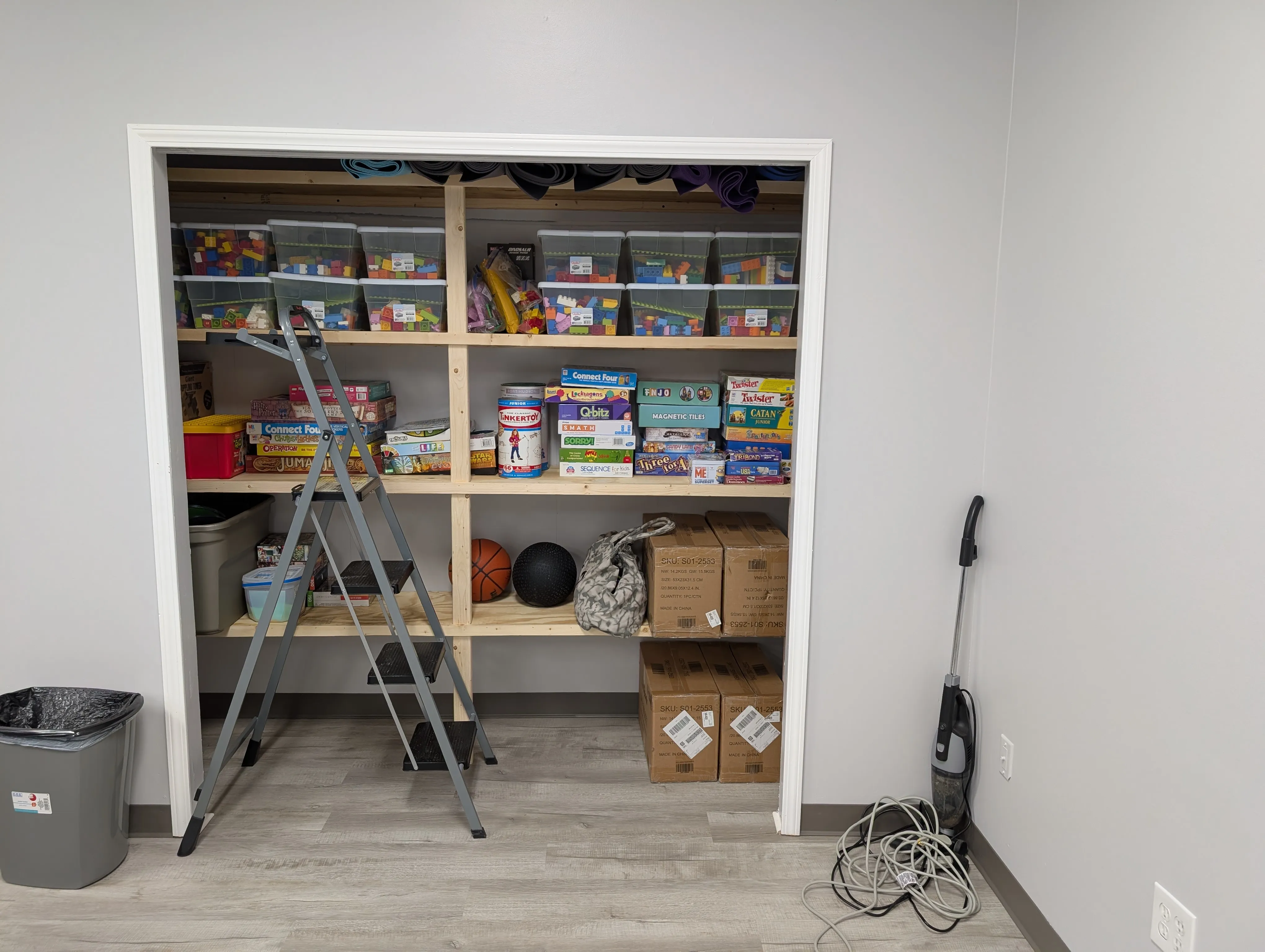 Open shelves stocked with bins of toys, board games, yoga mats, and supplies in the HUB.